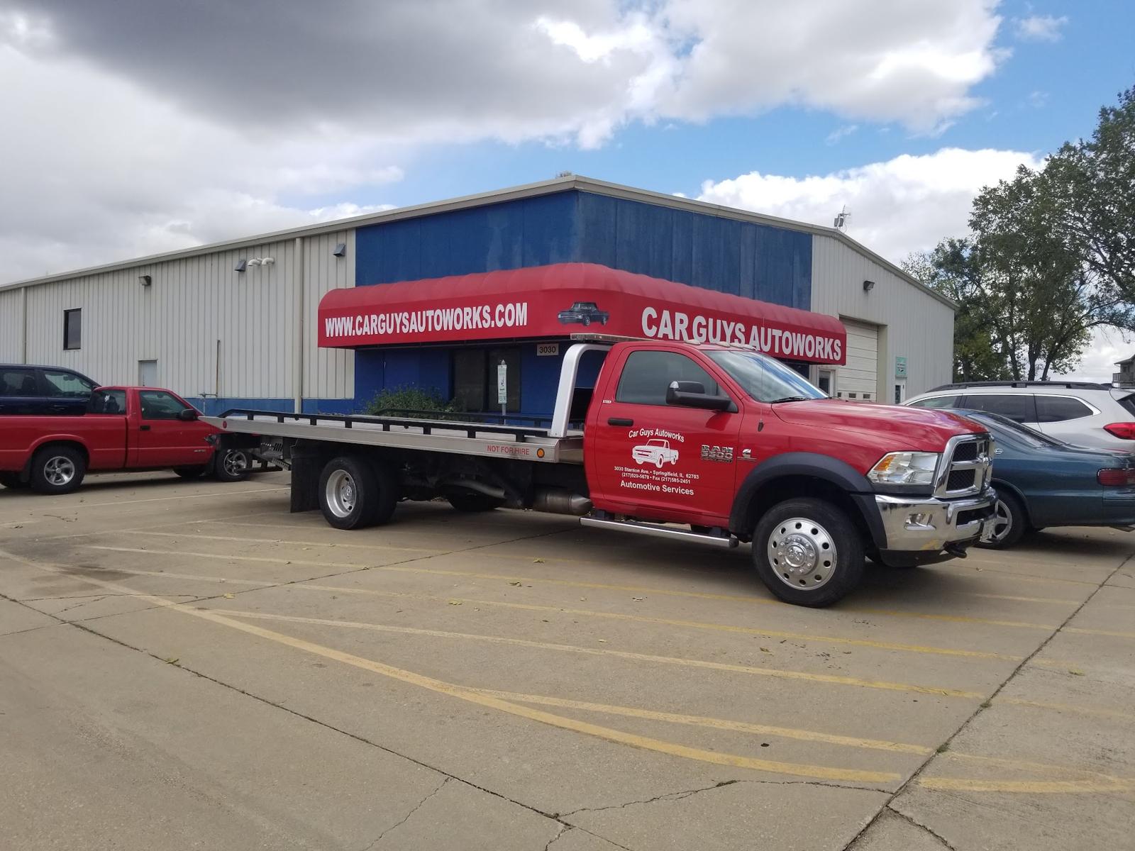 The red Car Guys Autoworks flatbed tow truck parked outside the shop